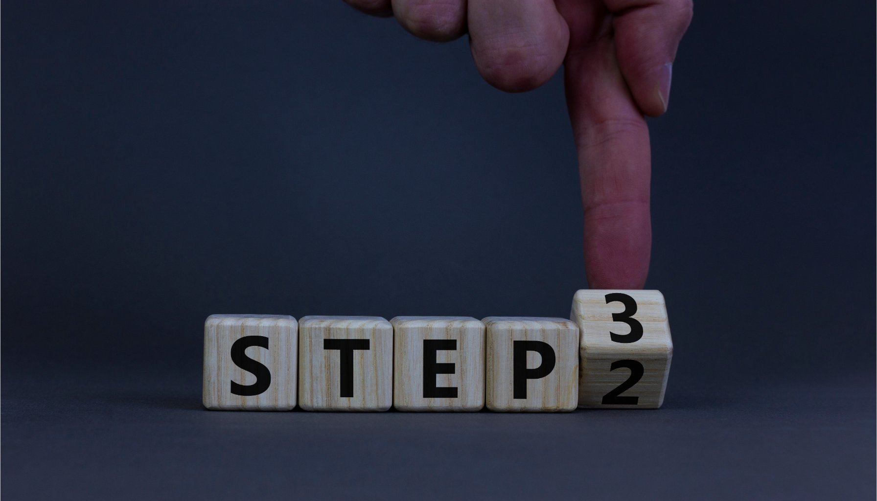 A hand flipping a wooden block from number 2 to number 3 to represent taking Step 3 in addiction recovery.